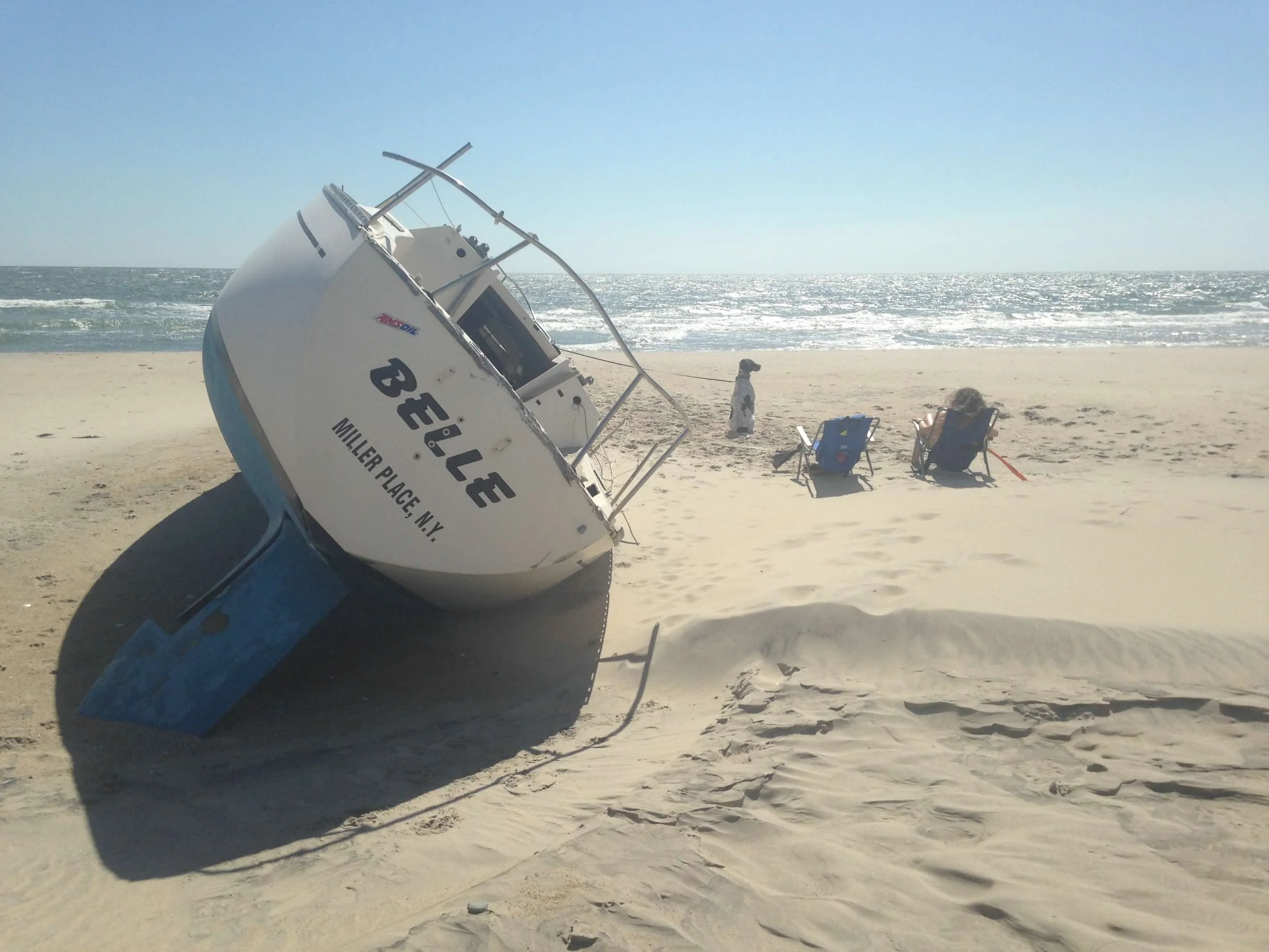 A sailboat named Belle wrecked and half-buried in sand on an Outer Banks beach