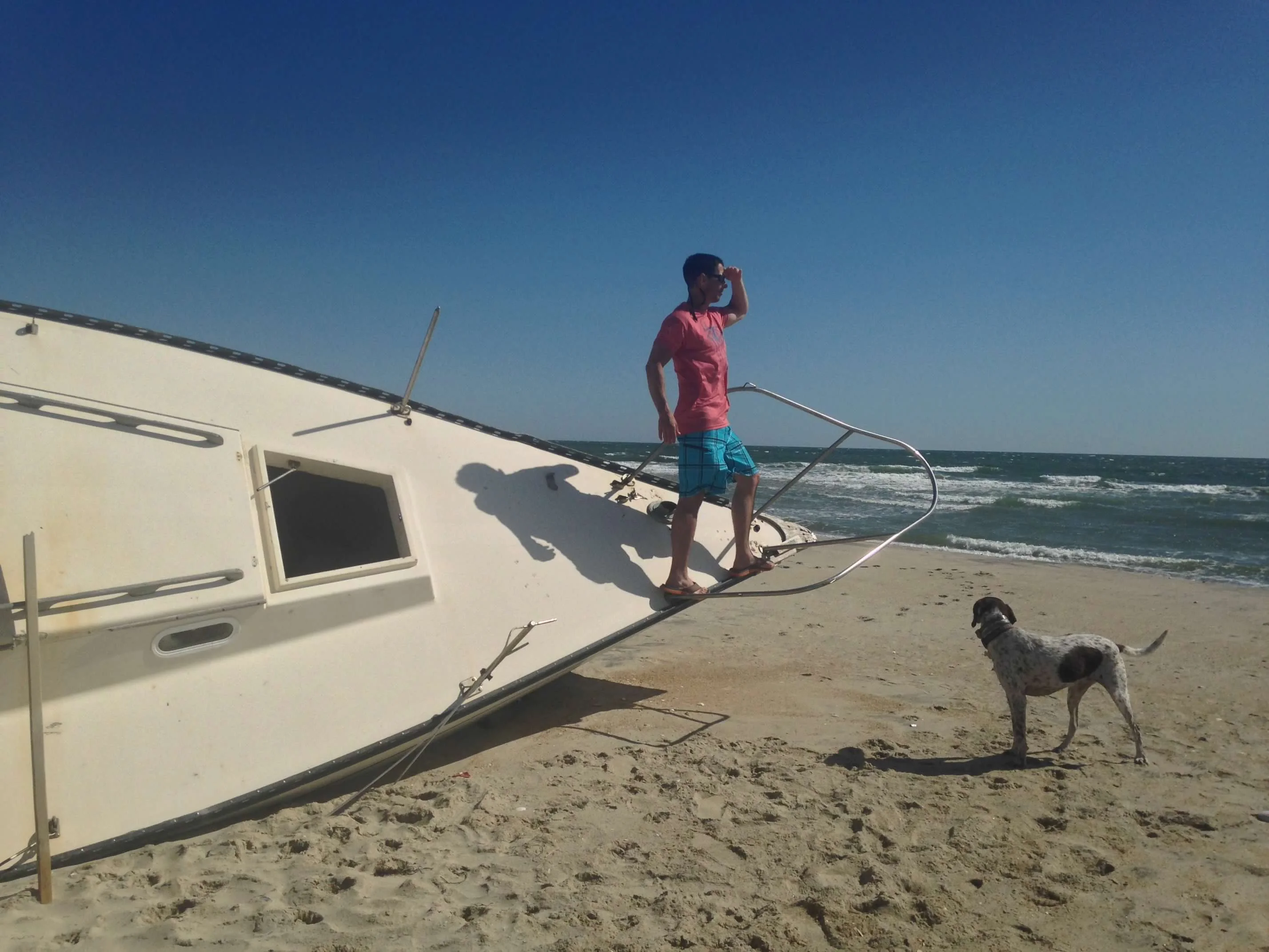 A man and dog standing on a sailboat wrecked and beached on an Outer Banks shore