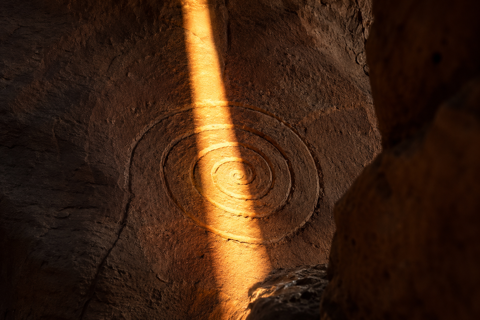 A shaft of light crossing a spiral petroglyph carved in sandstone, summer solstice solar calendar