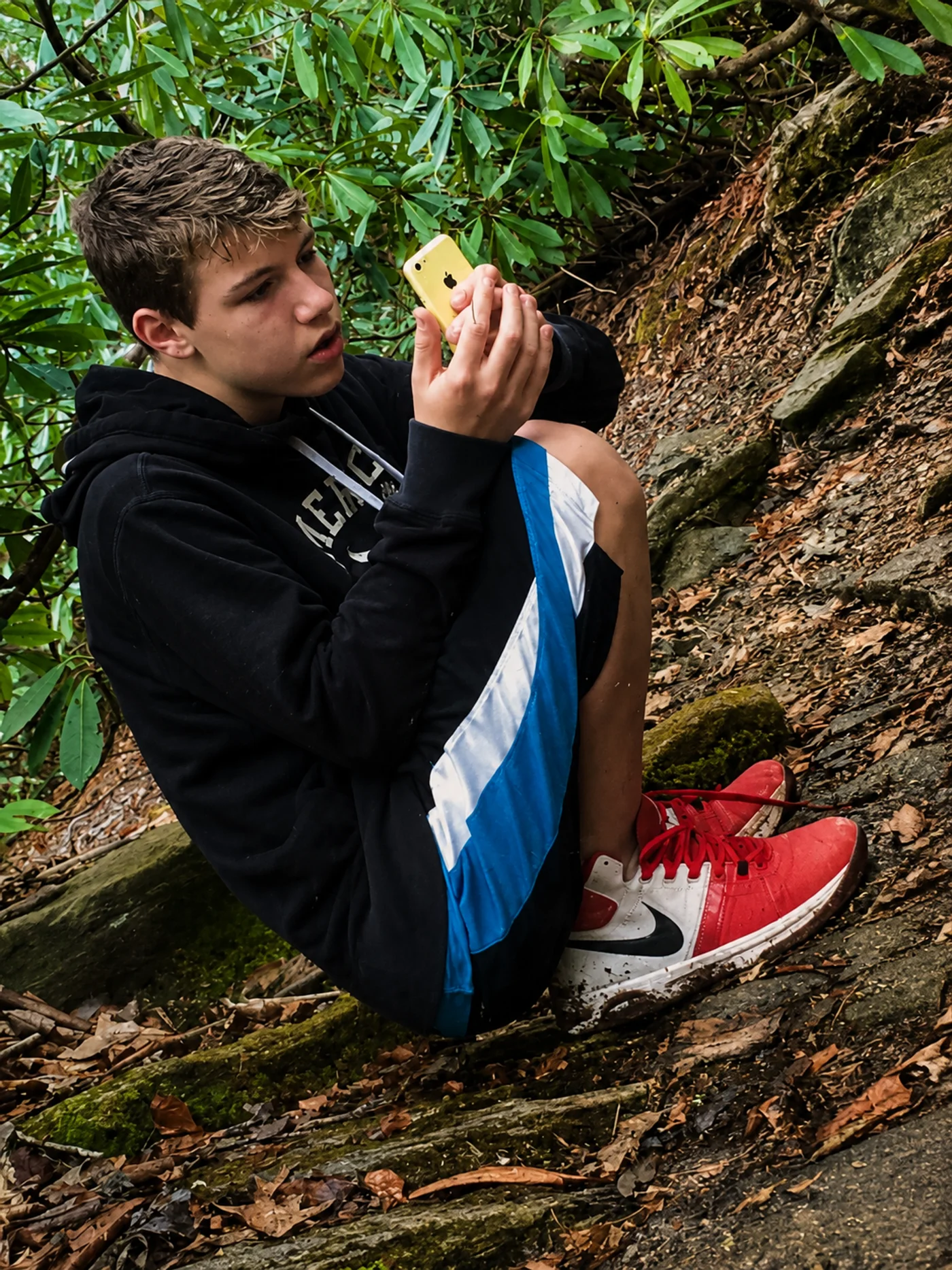 Zac in the North Carolina rhododendrons — sitting on the rocks, working the angle on his yellow iPhone