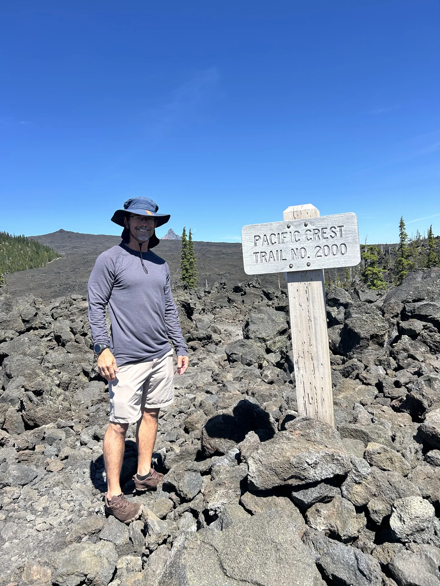 Tortuga at the Pacific Crest Trail No. 2000 marker on McKenzie Pass lava — one of the Three Sisters visible behind him